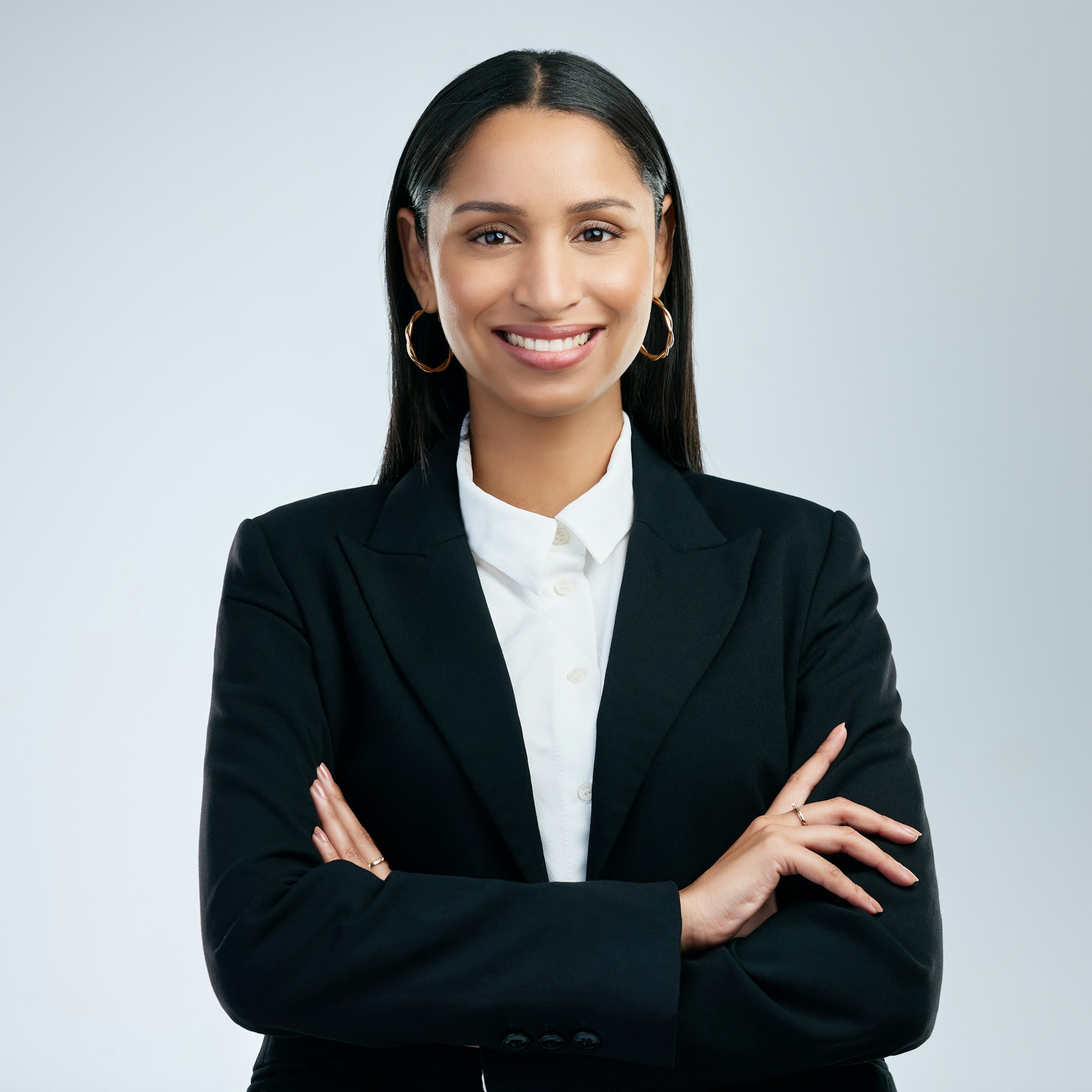 Confident professional woman in a black suit with arms crossed smiling.